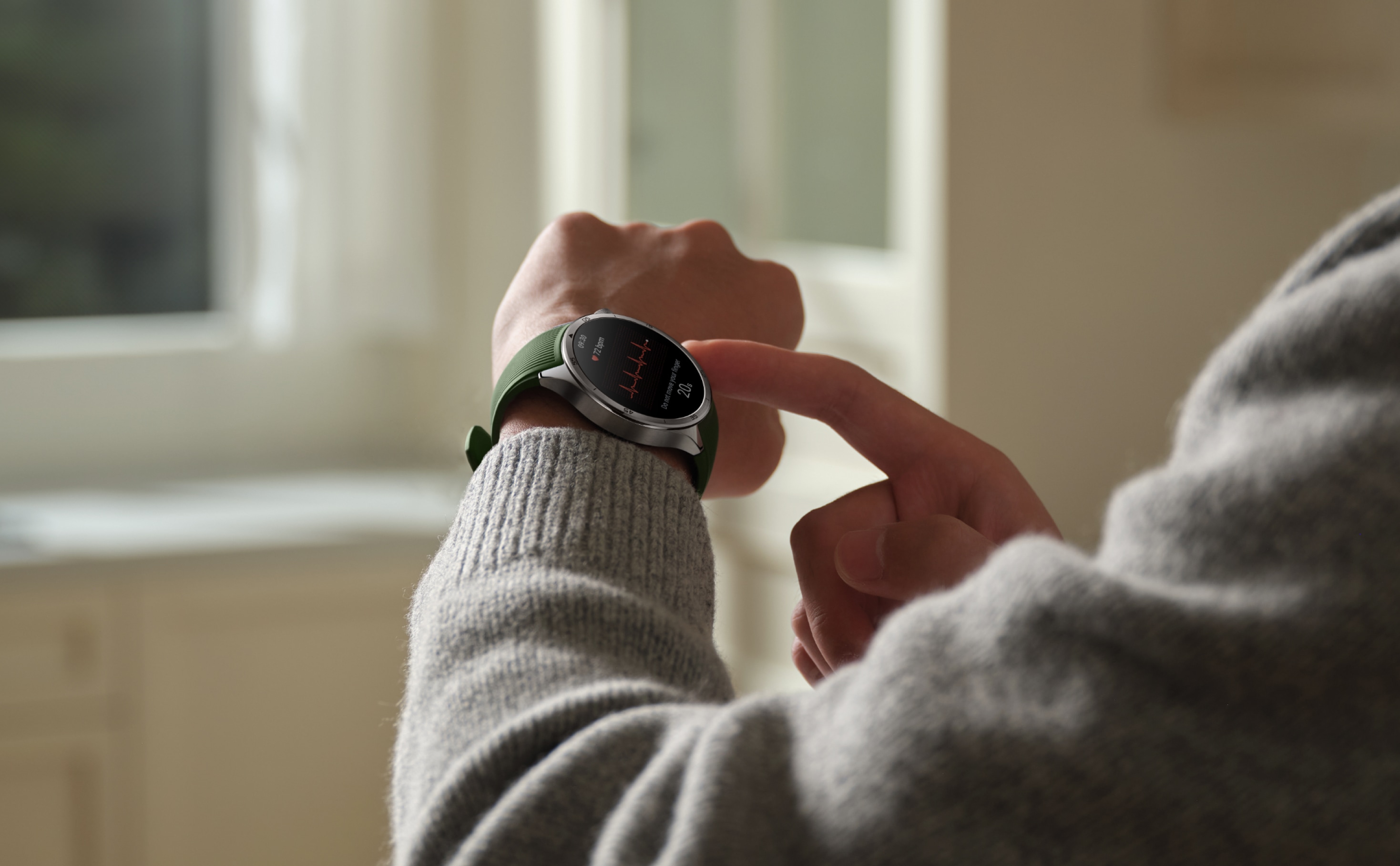 A person wearing a gray sweater with a smartwatch on their wrist displaying data.